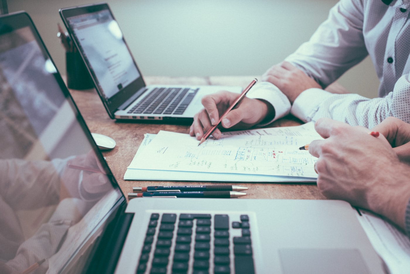 Dos asesores revisan cálculos y gráficos financieros sobre una mesa con computadoras portátiles.