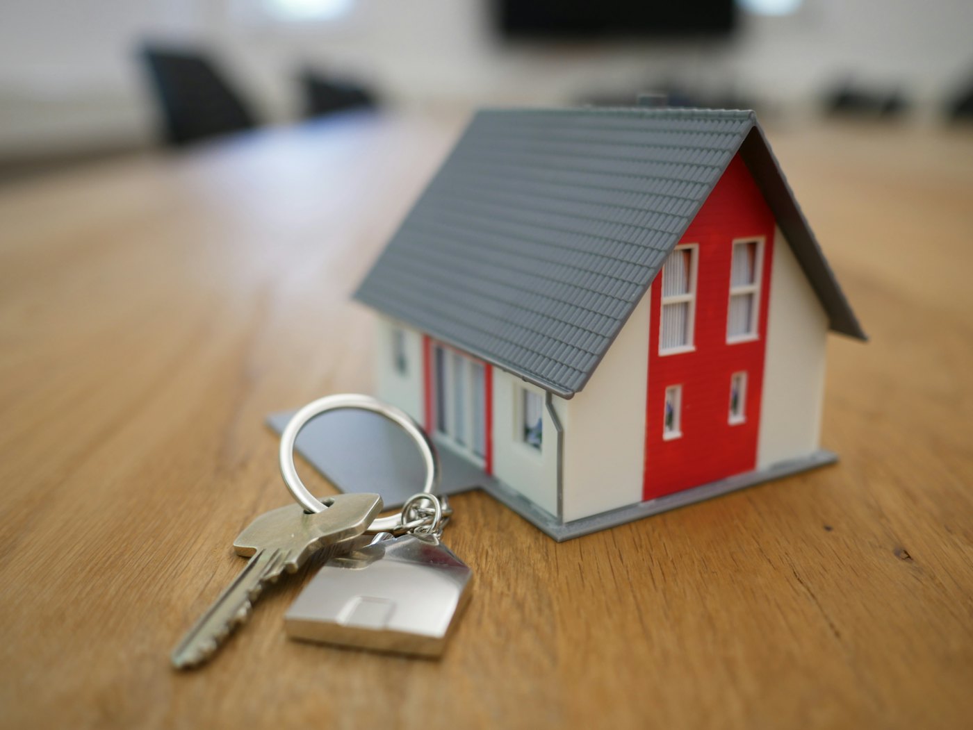 Llaves de una vivienda junto a una casa en miniatura sobre un escritorio de madera.