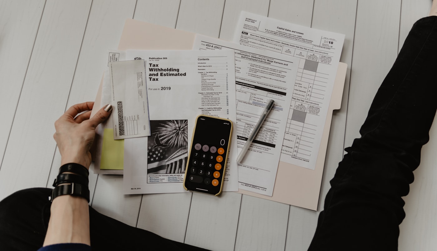 Formularios tributarios, una calculadora en el teléfono y documentos ordenados sobre una mesa blanca.