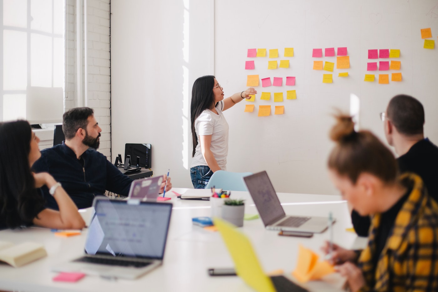 Facilitadora dirige un taller de planificación frente a una pizarra con notas adhesivas de colores.